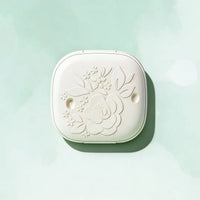 Morong close-up detail of the finely embossed camellia flower and bud pattern on the lid of the white, square compact box.